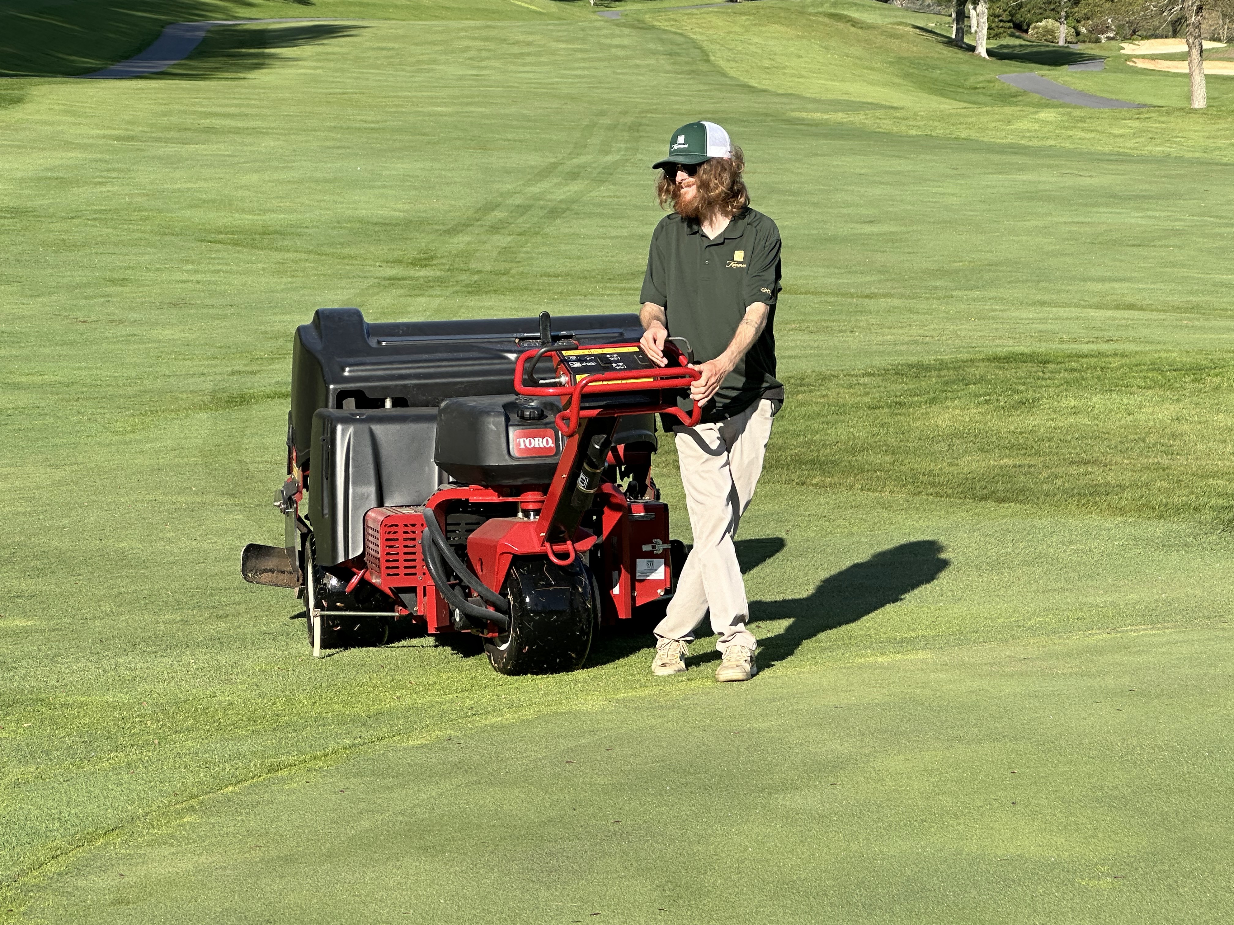 Close perspective of an operator guiding a Toro ProCore with visible rows of holes behind it.