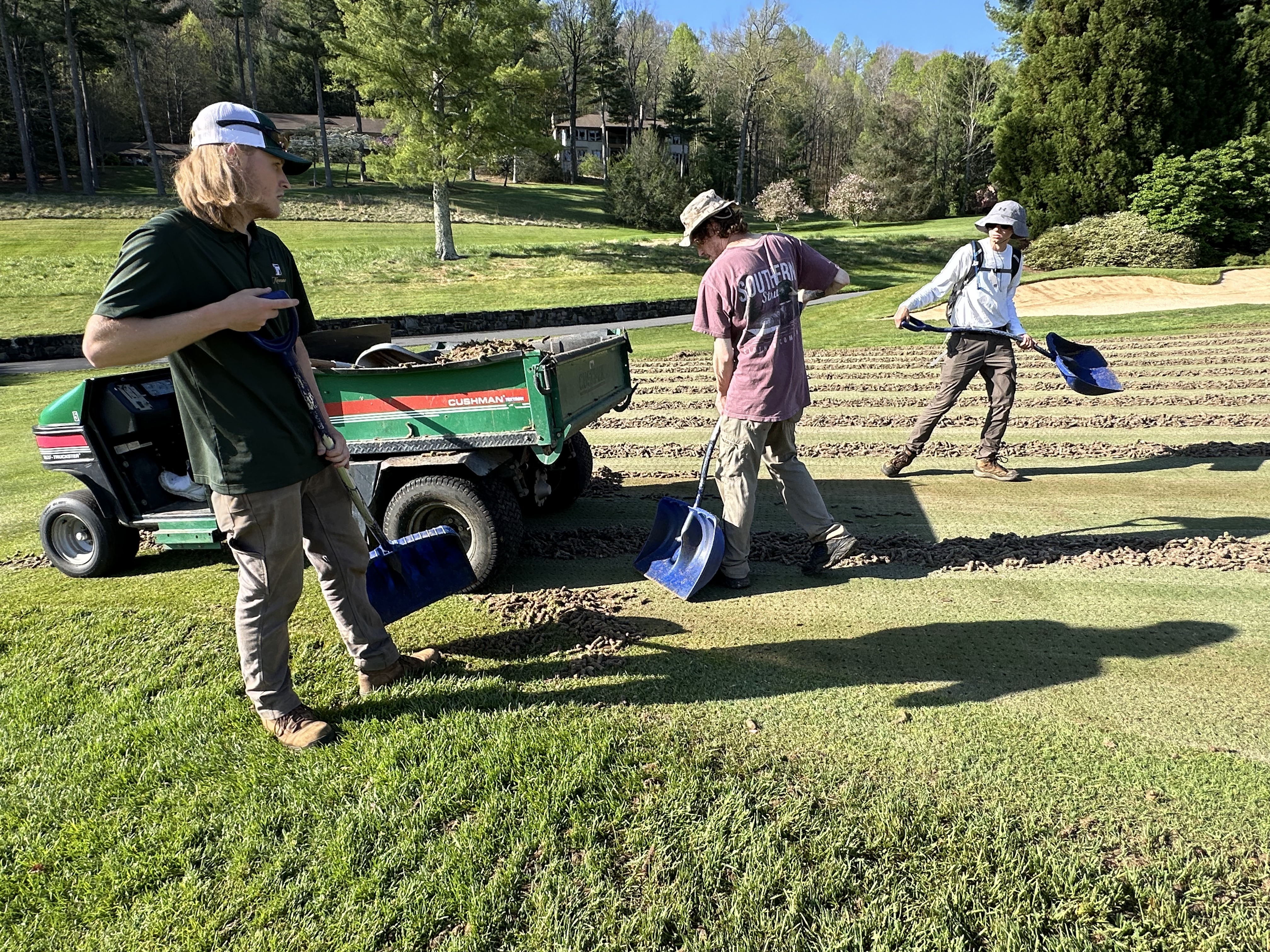 Three crew members spreading and clearing cores beside a green Cushman utility vehicle.